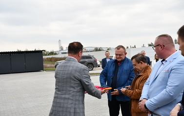 Burmistrz Pakości Zygmunt Groń podający nożyczki do uroczystego przecięcia wstęgi Przewodniczącemu Rady Miejskiej w Pakości